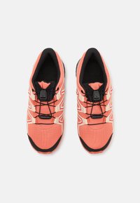 Coral running shoes with black accents, textured fabric, elastic laces, and a cushioned sole for comfort.