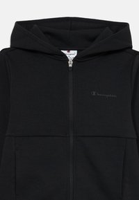 Svart zip-up hettegenser laget av mykt stoff med en frontlomme, justerbar hette og en diskret logo på brystet.