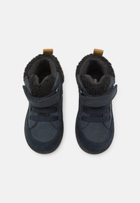 Námořnické modré kotníkové boty s semišovým vnějším povrchem, chlupatým černým podšitím, suchým zipem a elastickými šňůrkami. Gumová podrážka a hněhý úchyt.