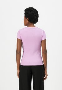 Korte mouwen, aansluitend t-shirt van lichtpaarse ribstof. Eenvoudige ronde halslijn en een gladde textuur, gecombineerd met zwarte wijde broek.
