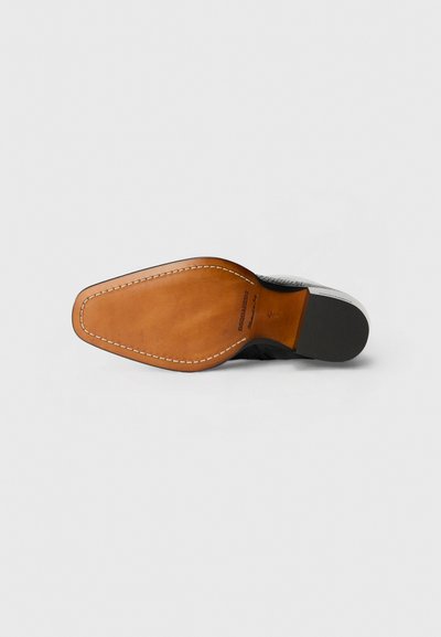 Suela de zapato con base de cuero marrón y parte superior texturizada en negro. Presenta costura a lo largo del borde y un tacón de goma negra suave.
