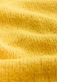 Dzeltena adīta auduma virsma ar mīkstu, teksturētu struktūru, kurai ir smalka ribota raksta un siltas, dzīvīgas krāsas tonis.