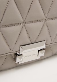Gros plan d’une surface en cuir matelassé beige avec des coutures triangulaires et une boucle argentée Michael Kors.