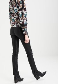 Mustat nahkahaalarit, joissa on sivuaukot, yhdistettynä moniväriseen kukkakuosisweateriin, jossa on teksturoitua kangasta ja mustia yksityiskohtia.