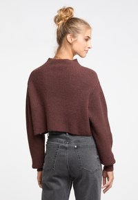 Gekürzter burgunderfarbener Pullover mit gerippter Textur und hohem Kragen, kombiniert mit grauen Jeans. Einfaches Design, keine sichtbaren Muster oder Akzente.
