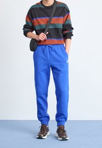 Striped sweater in black, green, and rust colors; blue sweatpants with elastic waistband; brown sneakers with white accents.