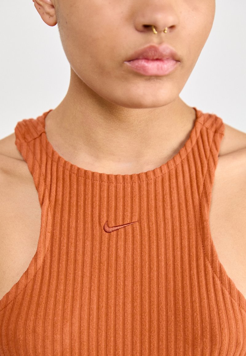 Top de tirantes acanalado de color óxido con un cuello alto, que presenta un pequeño logo bordado de Nike. Tejido texturizado con tirantes anchos.