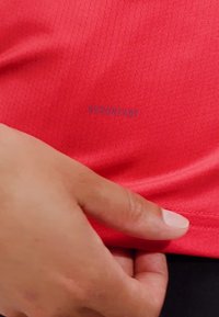 Maglietta sportiva rossa con un tessuto testurizzato e traspirante. Presenta un discreto dettaglio del marchio vicino all'orlo, con un design aderente.