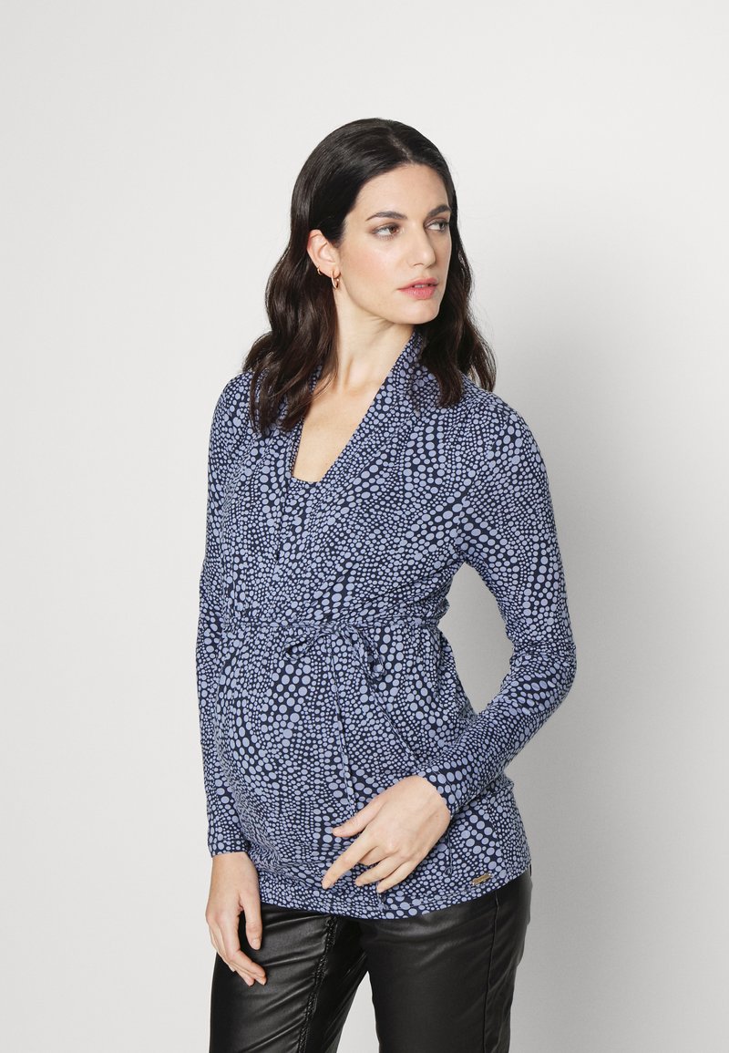 Top de maternidade em azul escuro com padrão de bolinhas azuis claras, mangas longas, design cruzado e detalhe franzido na cintura. Tecido suave.