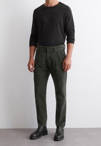 Tmavě šedé dlouhé rukávy tričko spárované se zelenými kordovými kalhotami. Kalhoty mají rovný střih a přední záhyby, doplněné černými kotníkovými botami.