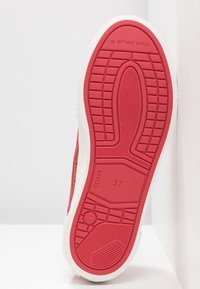 Baskets rouges avec semelle blanche, présentant une semelle extérieure texturée et un design minimaliste ; affiche la taille de chaussure 37 et le logo "G-STAR RAW."