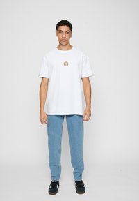 Hvid bomulds t-shirt med korte ærmer og rund halsudskæring, prydet med et lille multicolorlogo på brystet. Bæret sammen med lyseblå denimbukser.