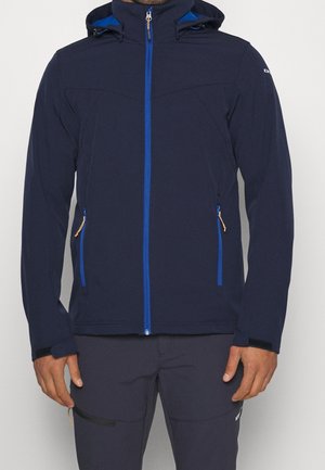 Uomo che indossa una giacca con cappuccio blu scuro con cerniera blu e tasche con cerniera, abbinata a pantaloni scuri.