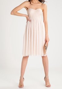 Sukienka bez ramiączek w kolorze różowym, z teksturowanym korpusem i falującą plisowaną spódnicą. W połączeniu ze złotą kopertówką i cielistymi szpilkami.