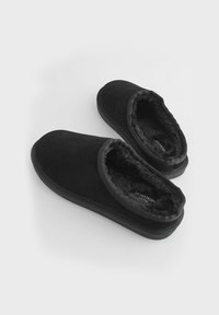 Schwarze Wildlederhausschuhe mit einem weichen, flauschigen Innenfutter, abgerundetem Zehenbereich und schlichtem Knöchelhöhen-Design. Flache Sohle für die Verwendung im Innenbereich.