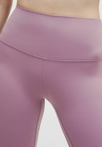 Legginsy z wysokim stanem w stonowanym lawendowym kolorze, charakteryzujące się gładką teksturą i detalami szwów po bokach, wykonane z elastycznego materiału.