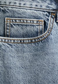 Poche de jean en denim bleu avec surpiqûre orange visible et texture du tissu en gros plan sur un matériau en denim délavé.