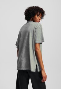 Grå oversized t-skjorte, mykt bomullsstoff, korte ermer, sideskår, svakt teksturert overflate, uformell og løstsittende design.