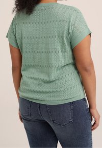 Suéter de manga corta color verde menta con un patrón de punto abierto texturizado. Cuello y dobladillo acanalados. Combinado con jeans azul oscuro.