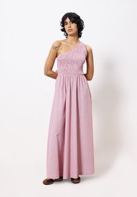 Robe rose à épaule unique avec corsage smocké et jupe fluide. Présente un motif texturé et atteint le sol, accompagnée de chaussures marron.