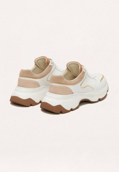 Zapatillas blancas y beige con suela gruesa, que presentan detalles de tela texturizada y sutiles costuras amarillas. Forma redondeada y diseño elegante.