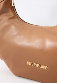Šviesiai ruda dirbtinės odos rankinė su apvalia forma, auksine užtrauktuku ir auksiniu "LOVE MOSCHINO" logotipu priekyje. Lygus paviršius su blizgiu finišu.