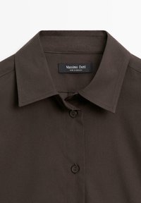 Donkerbruine overhemdbloes met een gestructureerde kraag, met een label dat "Massimo Dutti" vermeldt. Gemaakt van een gladde stof met een effen ontwerp.