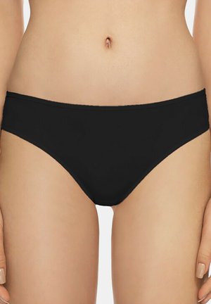 Femme portant un sous-vêtement style bikini noir, montrée de la taille jusqu'aux cuisses supérieures, les mains reposant sur les côtés.