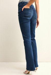 Dark blue denim jeans with a straight-leg cut, featuring two back pockets and a fitted waistband. Material appears smooth with slight texture.
