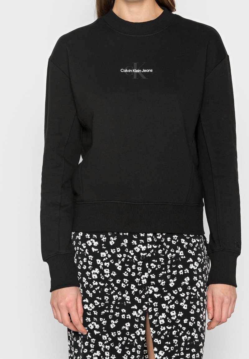 Sudadera negra de mezcla de algodón con cuello y puños acanalados. Presenta un logo blanco de "Calvin Klein Jeans" en el pecho.