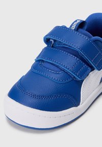 Baskets pour enfants bleues et blanches avec deux bandes Velcro ajustables et une semelle blanche texturée sur un fond uni.