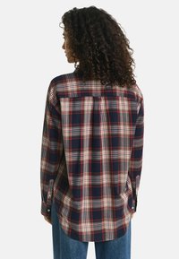 Geruite flanellen shirt in marineblauw, rood en crème; lange mouwen, knoopmanchetten en een gebogen zoom; voorzien van een schouderpas en zijsplitten aan de zoom.