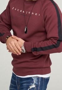 Bordowa bluza z kapturem z logo "JACK & JONES", czarnymi bocznymi wstawkami, ściągaczami na mankietach i luźnym krojem, zestawiona ze znoszonymi dżinsami.