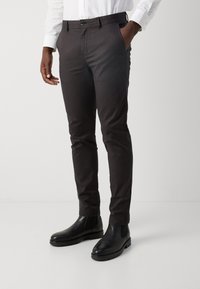 Pantalon gris foncé en mélange de coton, coupe slim, avec poches latérales et fermeture à bouton, associé à des bottines Chelsea noires.