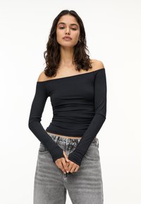 Sort, off-shoulder langærmet top med rynkedetaljer; bæres med lysegrå højtaljede jeans med en falmet tekstur.