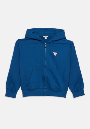 Sweat à capuche bleu zippé avec poches avant et petit logo triangulaire Guess sur la poitrine gauche.