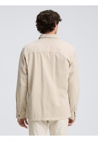 Lichtbeige knoopsluiting overhemd met een kraag, lange mouwen en een rechte zoom. Bevat een gladde textuur en een eenvoudig ontwerp met minimale details.