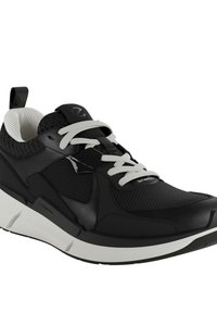 Svart idrottssko med ovandel i mesh, vita snören och vadderad krage. Sulan är tjock och vit med svarta accenter och logotyp.