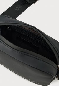 Μαύρη τσάντα crossbody με φερμουάρ, με υφή στην επιφάνεια και λογότυπο. Στο εσωτερικό περιλαμβάνει τσέπη με φερμουάρ και υφασμάτινη επένδυση.