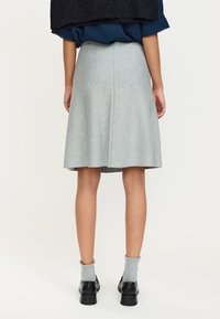 Gonna grigia a ruota in tessuto strutturato, con cucitura posteriore e orlo sottile. Abbinata a scarpe nere e calzini grigio chiaro.