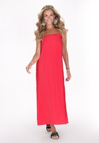 Abito maxi plissettato rosso con scollo smock, caratterizzato da una vestibilità ampia e spacchi laterali. Abbinato a sandali decorativi neri.
