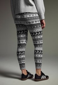 Sorte og hvide leggings med et mønstret design bestående af hjerter, renaer og træer. Sammen med en grå sweater og sorte sneakers.