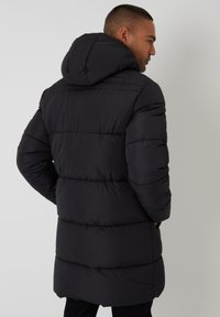 Black puffer jacket with a hood, featuring a quilted design, long cut, and elastic cuffs. Smooth texture with a lightweight appearance.