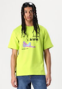 Limegrønn oversized t-skjorte i bomull, med trykket tekst og grafisk design. Korte ermer, avslappet passform og rund hals.