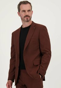 Bruine op maat gemaakte blazer met notch-lapels, enkele knoopsluiting en voorzakken. Draagt over een zwart shirt met een gestructureerde stof.