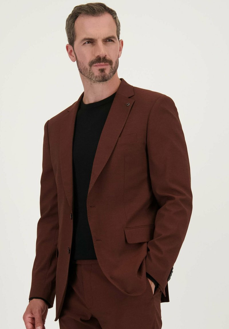 Bruine op maat gemaakte blazer met notch-lapels, enkele knoopsluiting en voorzakken. Draagt over een zwart shirt met een gestructureerde stof.