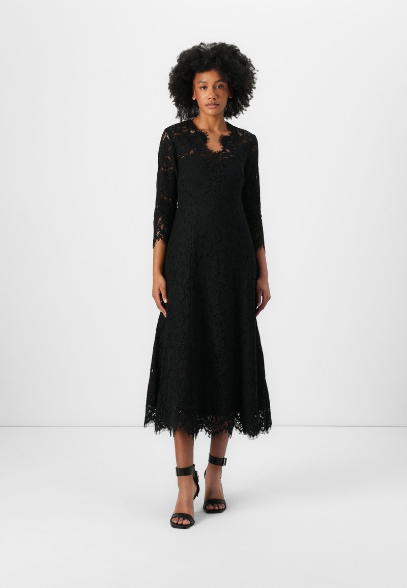 Robe en dentelle noire avec des manches trois-quarts et un ourlet en dentelle festonnée. Présente un décolleté en V et un motif floral en dentelle sur l'ensemble.