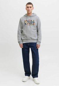 Sudadera gris con un logo gráfico multicolor en el frente, combinada con jeans de mezclilla oscura y zapatillas blancas. Tejido suave, con puños y dobladillo acanalados.