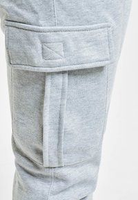 Lichtgrijze stof cargo zak met klep en stikdetails op een paar broek of joggingbroek.
