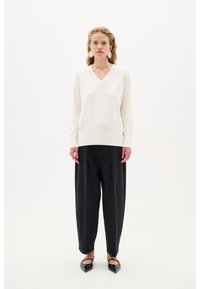 V-Ausschnitt Strickpullover in Elfenbein mit geripptem Saum, kombiniert mit schwarzen weit geschnittenen Hosen und spitzen schwarzen Ballerinas. Schlichte, klare Linien.